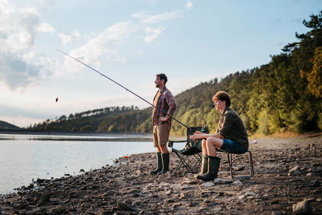 Father teaching teenage son to fish during outdoor trip. Teenage boy learning how to fish from his father. model released