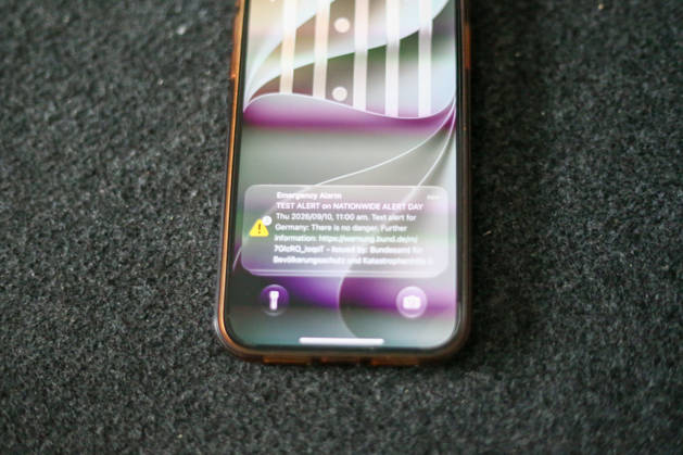 Germany, Europe: A smartphone lies on a dark surface, displaying a test alert on its lock screen for the nationwide Warning Day. The cell broadcast alert from the Federal Office for Civil Protection and Disaster Assistance (BBK) is visible on the screen. Stock image related to emergency warning systems, civil protection, crisis preparednes Copyright: xAymanxAlahmedx