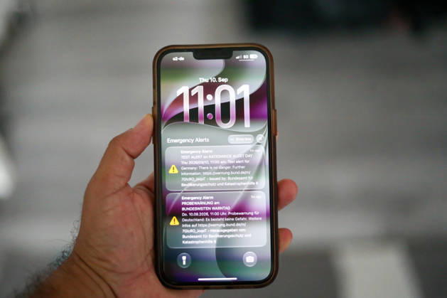 Germany, Europe: Close-up of a smartphone held in a hand, displaying a test alert for the nationwide Warning Day. The lock screen shows alerts from the Federal Office for Civil Protection and Disaster Assistance (BBK), as well as the time and date. Stock image related to disaster management, cell broadcast, warning systems, civil protection, and emergency c Copyright: xAymanxAlahmedx