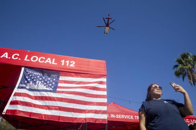 September 11, 2026, Los Angeles, California, USA: A woman takes photos next to a 9 11 remembrance flag during a helicopter flyover as the Los Angeles Fire Department marks the 25th anniversary of the terrorist attacks at the Frank Hotchkin Memorial Training Center in Los Angeles, California, on Sept. 11, 2026. Los Angeles USA  - ZUMAc68_ 20260911_zaf_c68_004 Copyright: xRingoxChiux