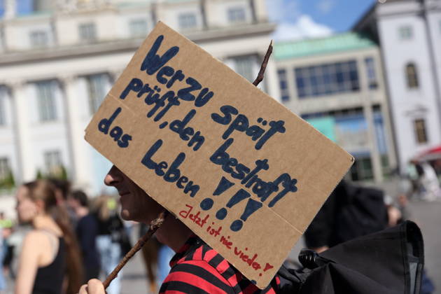 A protester holding a sign that reads, Life punishes those who wait too long to act. Now is never again, during a demonstration calling for the Federal Constitutional Court to review far-right parties, Alter Markt, Potsdam, September 12, 2026. Protest in Potsdam
