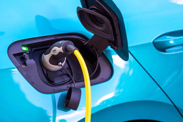 Close-up of the charging port on a turquoise electric car, with a yellow charging cable featuring a Type 2 Mennekes plug plugged into it