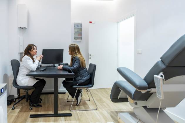 Ärztin, die mit einer jungen Frau über mögliche kosmetische Eingriffe oder Laser Haarentfernung spricht, sitzt an einem Schreibtisch in einer modernen ästhetischen Klinik mit sichtbarem Behandlungsstuhl Female doctor speaking with a young woman about potential cosmetic procedures or laser hair removal, sitting at a desk in a modern aesthetic clinic with a treatment chair visible Copyright: imageBROKER UnaixHuizi ibxuhu18825177.jpg ,model released, Symbolfoto ,property released