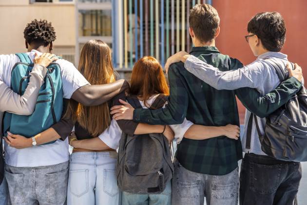 Gruppe multiethnischer Schüler, die mit umeinander geschlagenen Armen im Freien stehen und Freundschaft, Vielfalt und Zusammengehörigkeit in einem pädagogischen Umfeld symbolisieren Group of multi ethnic students standing outdoors with arms wrapped around each other, symbolizing friendship, diversity, and togetherness in an educational setting Copyright: imageBROKER UnaixHuizi ibxuhu19078224.jpg ,model released, Symbolfoto ,property released
