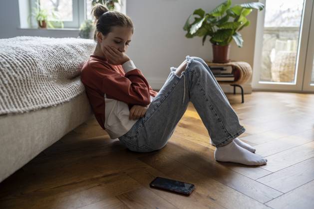 Das beleidigte unglückliche Teenager Mädchen schaut traurig auf das Telefon und sitzt zu Hause auf dem Boden. Trauriges, nachdenkliches, besorgtes Schulmädchen, das nach der Trennung von einem geliebten Jungen oder einem verletzenden Beitrag in den sozialen Medien an Depressionen leidet Offended unhappy teenage girl sadly looking at phone sits on floor at home. Sad thoughtful worried schoolgirl experiencing depression after breaking up with beloved boy or hurtful social media post Copyright: imageBROKER DimaBerlin ibxqgx18878376.jpg ,model released, Symbolfoto ,property released