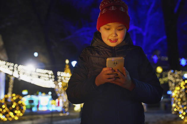 Smiling girl using smartphone outdoors at night with Christmas lights model released, Symbolfoto, AZF01532