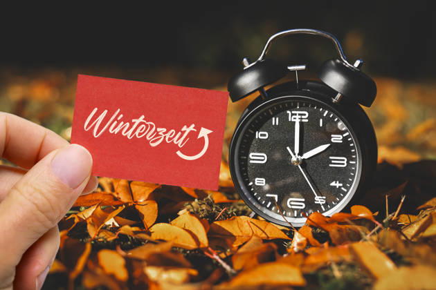 PHOTOMONTAGE: A hand holding a note that reads Winter Time in front of an alarm clock amid autumn leaves; symbolic photo of the time change in Hamburg, Germany ** FOR EDITORIAL PURPOSES ONLY ** EDITORIAL USE ONLY **