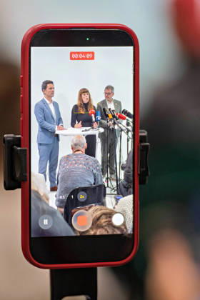 Berlin, October 8, 2026: Steffen Krach (SPD, left), Kerstin Wolter Ehling (Die Linke, M, and Werner Graf of Alliance 90 The Greens (right) can be seen on a smartphone screen during a joint press statement following the conclusion of their parties’ preliminary talks in the foyer of the Haus der Statistik. Press statement by The Left, The Greens, and the SPD in Berlin