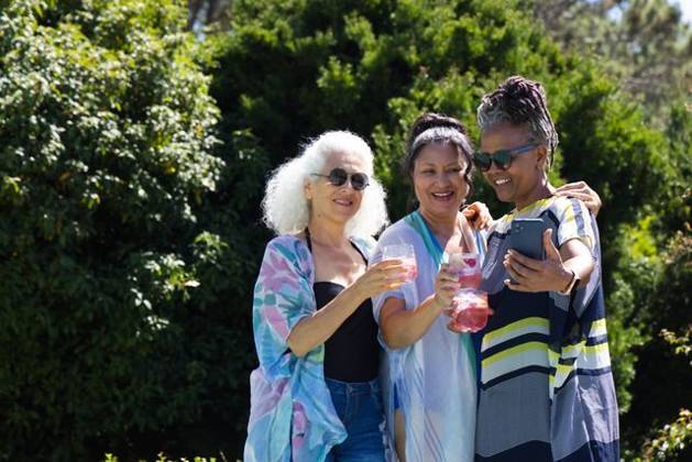 Diverse female friends posing for selfie in garden wearing coverups holding smartphone, pink drinks, model released, property released, 20.02.2026 06:00:00, 16229836 Copyright: xIDS-261006_1xcreatorid:x0x 16229836