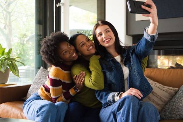 Diverse female friends posing for selfie on leather sofa in modern living room, holding smartphone, model released, property released, 21.05.2026 06:00:00, 16472232 Copyright: xIDS-261006_1xcreatorid:x0x 16472232