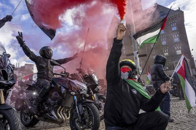 October 11, 2026, Amsterdam, Noord-Holland, The Netherlands: October 11, 2026, Amsterdam, Netherlands: A demonstrator crouches beside motorcycles and raises a canister emitting red smoke during a pro-Palestinian protest at Dam Square. A motorcyclist behind them raises both arms. Amsterdam The Netherlands - ZUMAl165 20261011_zip_l165_013 Copyright: xOrinxLouisx