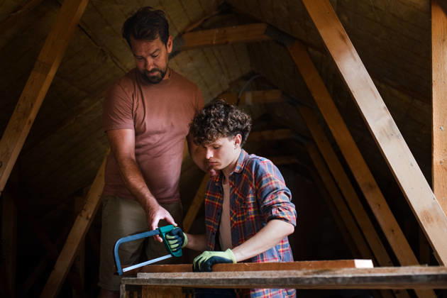 Father teaching teenage son DIY skills while renovating attic together. Dad and teenage son working together on home renovation project. model released