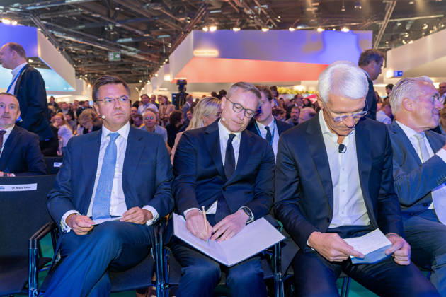 Berlin, 13.10.2026: Der portugiesische Minister Goncalo Saraiva Matias, Bundesdigitalminister Karsten Wildberger, der sich Notizen macht, und Bitkom-Präsident Ralf Wintergerst, der auf eine Karteikarte blickt (von links), sitzen vor Beginn des Bühnenprogramms in der ersten Reihe der Smart Country Convention in der Halle hub27; links steht ein für Messe-Chef Dr. Mario Tobias reservierter Stuhl. Portugal ist Partnerland der Smart Country Convention 2026 und präsentiert dort seine Erfahrungen mit der Digitalisierung der öffentlichen Verwaltung. Ralf Wintergerst ist seit 2023 Präsident des Digitalverbands Bitkom. Karsten Wildberger ist seit Mai 2025 Bundesminister für Digitales und Staatsmodernisierung und leitet das damals neu geschaff