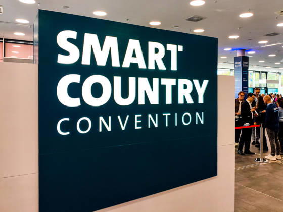 Large, illuminated logo for the Smart Country Convention (SCCON) in the entrance area of Messe Berlin. Visitors and industry professionals stand at the entrance to the Smart Country Convention (SCCON 2026) trade show, Berlin, trade fair, digitization, digital policy, smart city, smart Copyright: xJulianxCunowx