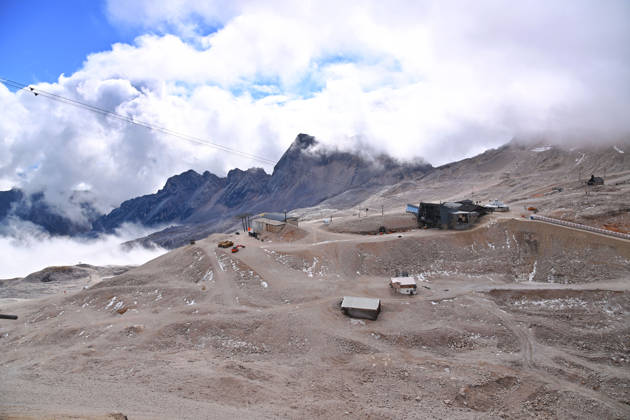 View across the rocky Zugspitzplatt with station buildings, mountain huts, and approaching banks of clouds. Ski resort: The shrinking Schneeferner Glacier on the Zugspitzplatt beneath a thick blanket of clouds