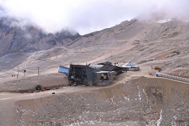 View across the rocky Zugspitzplatt with station buildings, mountain huts, and approaching banks of clouds. Ski resort: The shrinking Schneeferner Glacier on the Zugspitzplatt beneath a thick blanket of clouds