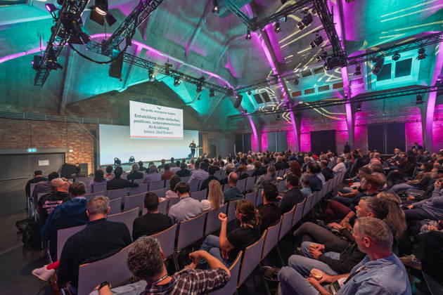 Berlin, 16.10.2026: Zahlreiche Zuhörer verfolgen in der violett und türkis beleuchteten Halle des WECC den Vortrag des Publizisten und Digital-Vordenkers Sascha Lobo auf der NeulandPro Connect 2026. Die zweitägige KI-Konferenz NeulandPro Connect 2026 findet am 16. und 17. Oktober im Westhafen Event & Convention Center (WECC) in Moabit statt, einem historischen Speichergebäude am Berliner Westhafen. Veranstalter ist NeulandPro, eine Bildungs- und Medienmarke rund um Künstliche Intelligenz. Mit Vorträgen, Workshops und Hackathons richtet sich die Konferenz vor allem an kleine und mittelständische Unternehmen, Gründer und Führungskräfte, die KI praktisch einsetzen wollen; erwartet werden bis zu 1.000 Gäste. NeulandPro Connect 2026 -