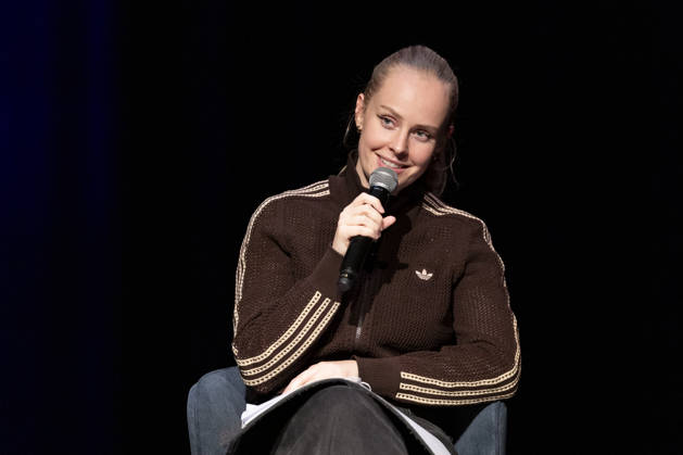 Poetry artist and author Clara LOESEL LÖSEL, smiling during her reading—a preview event for her new book, *Ich dachte, sowas fühle nur ich*—seated with a microphone; single frame, single photo, at the Theater am Tanzbrunnen, Cologne, on October 23, 2026