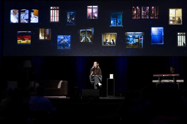 Poetry artist and author Clara LOESEL LÖSEL on stage during her reading—a preview show for her new book, *Ich dachte, sowas fühle nur ich*—seated with a microphone, accompanied by piano; single frame, single photo, at the Theater am Tanzbrunnen, Cologne, on October 23, 2026