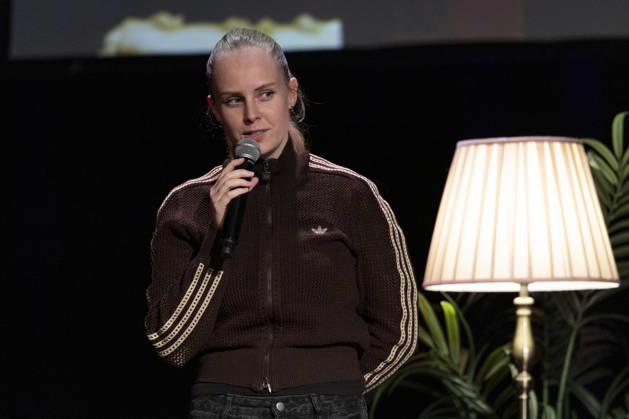 Poetry artist and author Clara LOESEL LÖSEL speaks intently during her reading—a preview of her new book, *Ich dachte, sowas fühle nur ich*—standing with a microphone, in a single frame, a single photograph, at the Theater am Tanzbrunnen, Cologne, on October 23, 2026