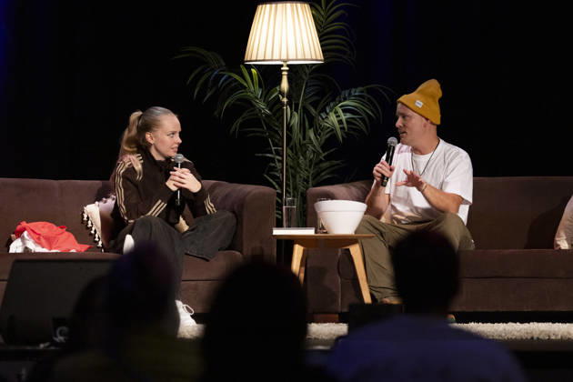 Poet and author Clara LOESEL LÖSEL (left) in conversation with author and podcaster Lars AMEND (right) during her reading—a preview event for her new book, *Ich dachte, sowas fühle nur ich*—sitting on sofas with microphones at the Theater am Tanzbrunnen, Cologne, on October 23, 2026