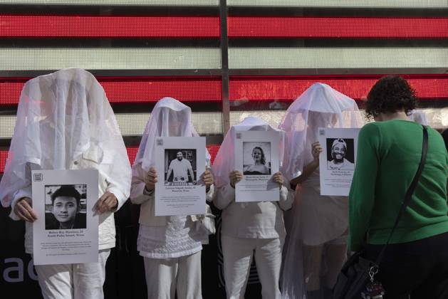 October 25, 2026, New York, New York, USA: A passerby stops to observe people dressed in white shrouds, Human Beings, memorializing those killed by gun violence from Federal immigration agents by holding signs with the images and names of Ruben Ray Martinez Lorenzo Salgado Araujo Renee Nicole Good Keith Porter Jr. Demonstrators with the anti-gun violence organization Gays Against Guns protest under the Times Square US Army Recruiting Station LED American flag to denounce U.S. Immigration and Customs Enforcement (ICE,) President Trump s immigrant detention and mass deportation policies. New York USA  - ZUMAr174 20261025_znp_r174_012 Copyright: xGinaxMxRandazzox